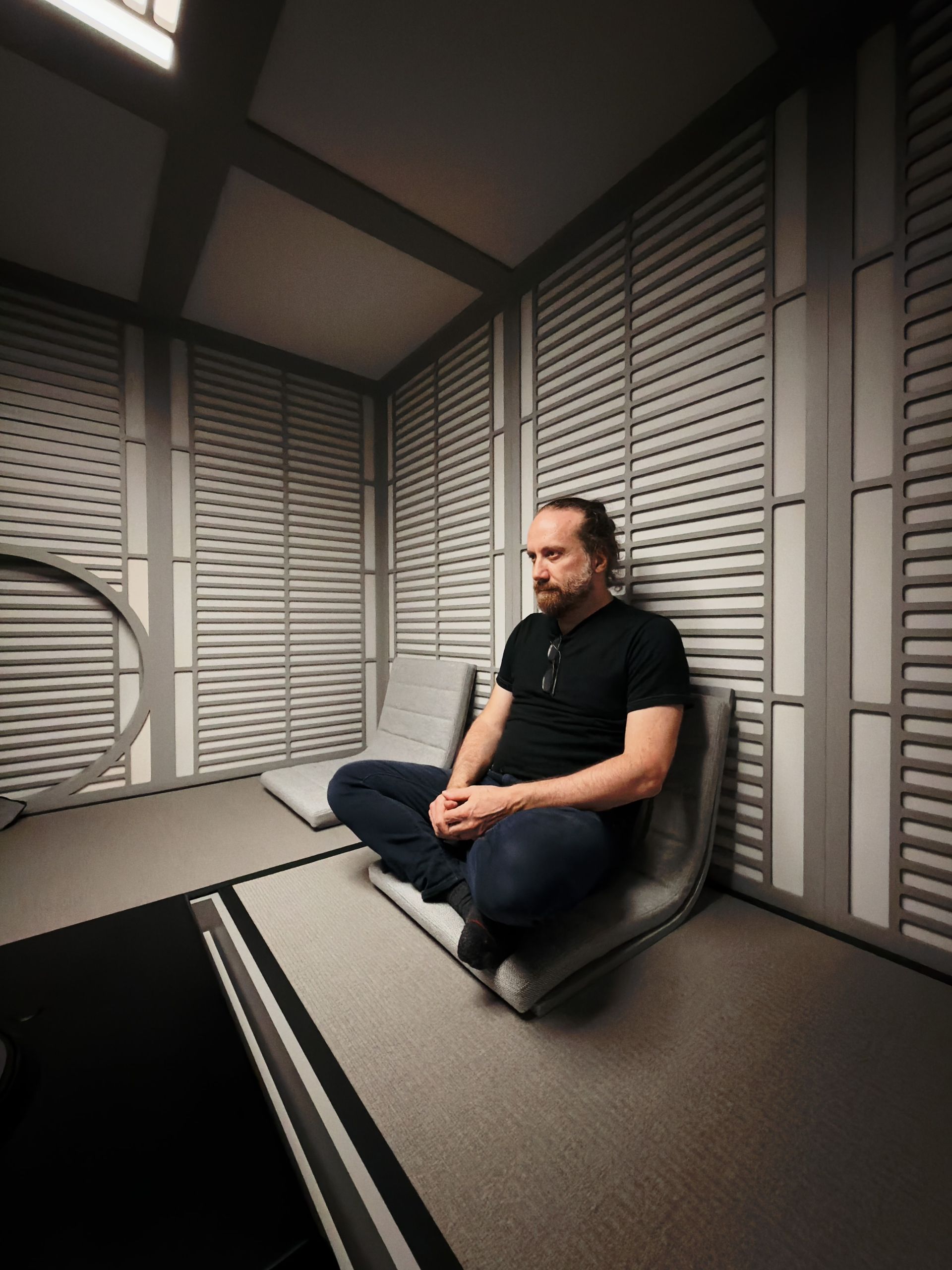 François seated cross-legged on a low cushioned seat in a Japanese interior with slatted wood walls, looking to the side.